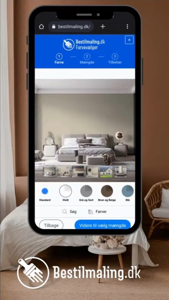 En mobiltelefon viser en app til farvevalg fra BestilMaling.dk. Telefonen er placeret foran en seng i et stilrent soveværelse. Tekst på skærmen: Bestilmaling.dk Farvevælger.